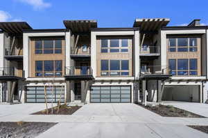 Modern home with driveway, stone siding, a balcony, and a garage