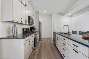 Kitchen featuring stainless steel appliances, white cabinets, light wood-style floors, decorative backsplash, and recessed lighting