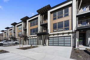 View of front of property with concrete driveway, stone siding, an attached garage, and a balcony
