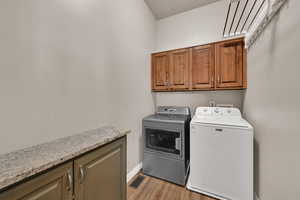 Laundry area with cabinet space, washing machine and clothes dryer, light wood-type flooring, and a textured ceiling