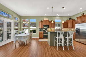 Kitchen with brown cabinetry, stainless steel appliances, a kitchen bar, a chandelier, and backsplash