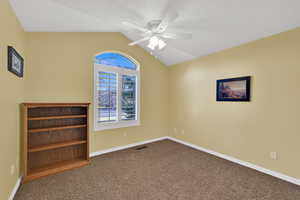Carpeted empty room with vaulted ceiling, ceiling fan, and a textured ceiling