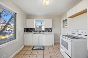 Kitchen with white appliances, white cabinetry, light tile patterned floors, light countertops, and tasteful backsplash