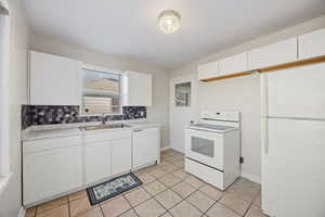 Kitchen with white cabinets, white appliances, light countertops, and backsplash