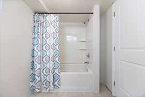 Bathroom with shower / bath combination with curtain, a textured ceiling, and light tile patterned floors