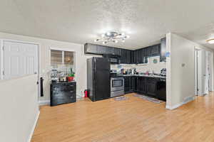 Kitchen with dark cabinetry, black appliances, light wood-style flooring, a textured ceiling, and light countertops