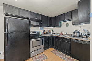 Kitchen featuring dark cabinets, black appliances, a textured ceiling, and light wood finished floors