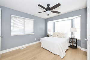 Bedroom with light wood-style flooring, ceiling fan, and multiple windows