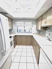 Kitchen view, white appliances, taupe cabinetry,  tile floors, with window out to balcony.