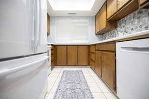 Kitchen with white appliances, light countertops, brown cabinets, light tile patterned flooring, and tasteful backsplash