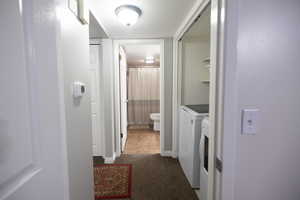 Hallway featuring dark colored carpet and washing machine and clothes dryer
