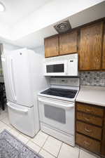 Kitchen with white appliances, light countertops, tasteful backsplash, light tile patterned floors, and brown cabinetry