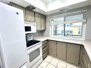 Kitchen with taupe painted cabinetry, white appliances, light countertops, and tile floors