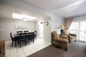 Dining area featuring light tile patterned flooring, a skylight, and light colored carpet