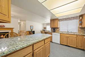 Kitchen with tasteful backsplash, light stone countertops, dishwasher, a tile fireplace, and light carpet