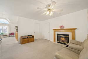 Living area featuring light carpet, a tiled fireplace, and a ceiling fan