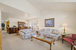 Carpeted living room featuring a chandelier and vaulted ceiling