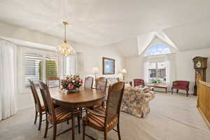 Dining area with vaulted ceiling, light colored carpet, and a chandelier
