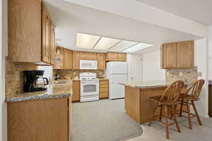 Kitchen featuring tasteful backsplash, white appliances, light stone countertops, and a peninsula