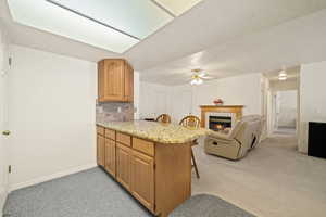 Kitchen featuring a kitchen bar, light carpet, a peninsula, a tiled fireplace, and open floor plan