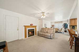 Living room featuring light carpet, a tiled fireplace, and a ceiling fan