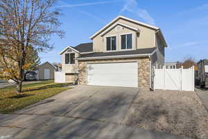 View of front facade with stone siding, a gate, concrete driveway, an attached garage, and a shingled roof