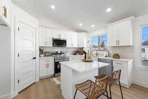 Kitchen featuring lofted ceiling, appliances with stainless steel finishes, white cabinets, tasteful backsplash, and recessed lighting