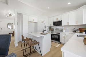 Kitchen featuring a breakfast bar area, stainless steel appliances, white cabinetry, a kitchen island, and vaulted ceiling