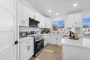 Kitchen with stainless steel appliances, white cabinetry, recessed lighting, light stone countertops, and light wood finished floors