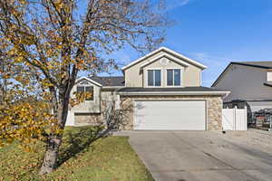 View of front of property featuring stone siding, an attached garage, driveway, and stucco siding