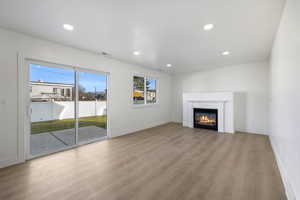 Unfurnished living room with light wood finished floors, a glass covered fireplace, and recessed lighting