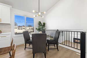 Dining area featuring a chandelier, a glass covered fireplace, light wood-style flooring, and high vaulted ceiling