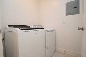 Laundry room featuring electric panel, washer and clothes dryer, and light tile patterned floors