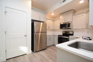 Kitchen featuring stainless steel appliances, light wood-type flooring, light stone countertops, white cabinetry, and recessed lighting