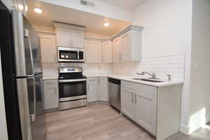 Kitchen with stainless steel appliances, light stone counters, light wood finished floors, decorative backsplash, and recessed lighting
