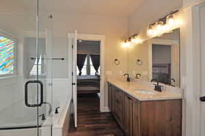 Bathroom featuring connected bathroom, double vanity, dark wood finished floors, a bath, and a shower stall