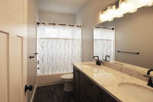 Full bathroom featuring double vanity, shower / bath combo, and dark wood-style floors