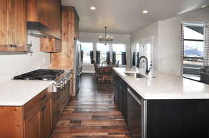 Kitchen featuring light stone countertops, appliances with stainless steel finishes, a kitchen island with sink, recessed lighting, and decorative light fixtures