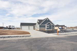 Craftsman-style house with stone siding, concrete driveway, a garage, board and batten siding, and a shingled roof