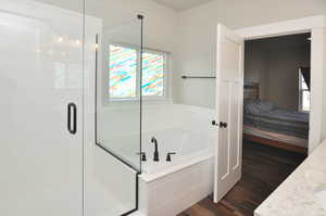 Ensuite bathroom with dark wood finished floors, vanity, a bath, and a stall shower