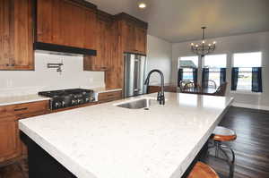 Kitchen with dark wood finished floors, stainless steel appliances, an island with sink, decorative light fixtures, and a chandelier