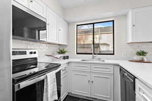 Kitchen with stainless steel appliances, white cabinetry, light stone counters, and tasteful backsplash
