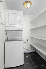 Laundry area featuring dark tile patterned floors, stacked washer and clothes dryer, and a textured ceiling