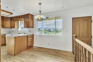 Kitchen featuring brown cabinets, decorative light fixtures, light countertops, a chandelier, and a peninsula