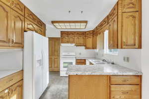 Kitchen featuring white appliances, light countertops, brown cabinets, a peninsula, and light tile patterned floors