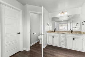 Full bathroom with double vanity, dark wood-style floors, and a stall shower