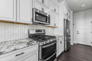 Kitchen with appliances with stainless steel finishes, white cabinets, light stone countertops, and dark wood-type flooring