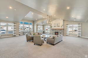 Living room with light carpet, a stone fireplace, vaulted ceiling, a chandelier, and recessed lighting
