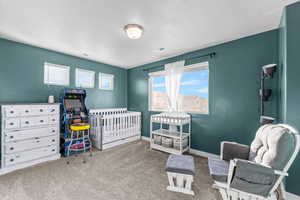 Bedroom with light colored carpet, a nursery area, and a textured ceiling