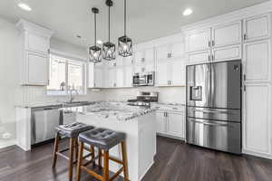 Kitchen with stainless steel appliances, decorative backsplash, decorative light fixtures, a breakfast bar area, and light stone countertops